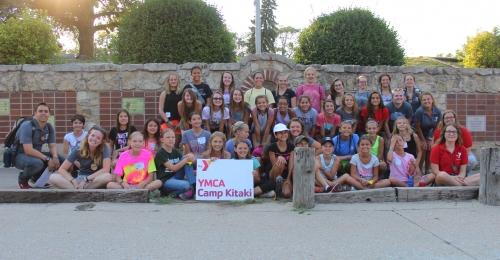 Participants in Camp Kitaki's ranch camp pose in front of the brick wall at camp