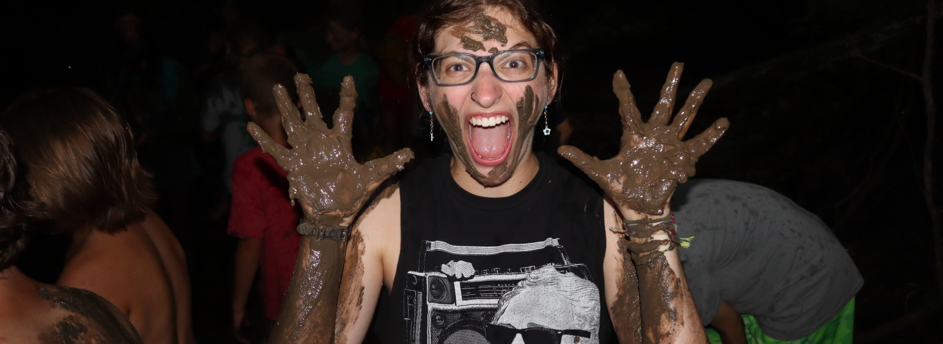 Camp Staff Member smiles at the camera with face and hands covered in mud