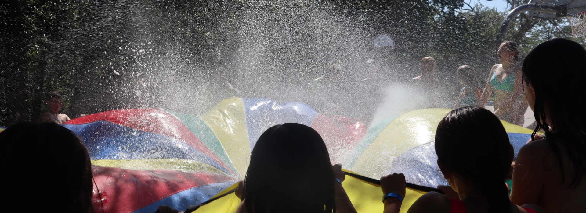 Silhouette of campers playing with giant parachute and water
