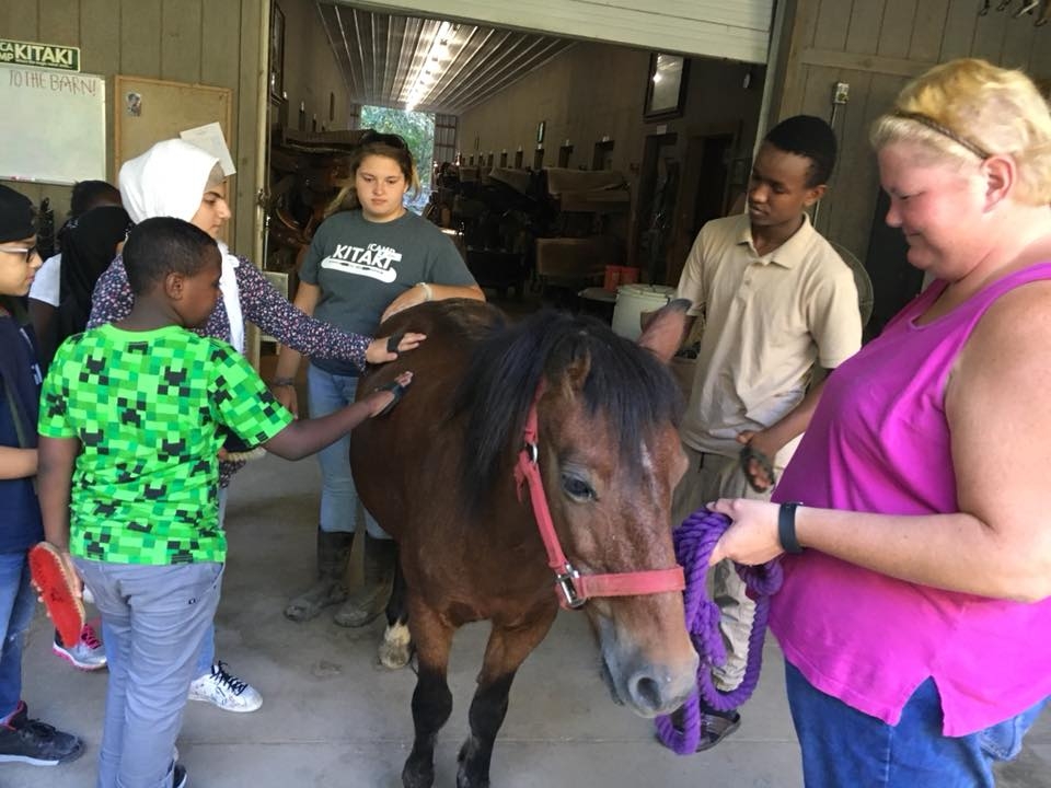 A staff holds a pony while members of a family pet it