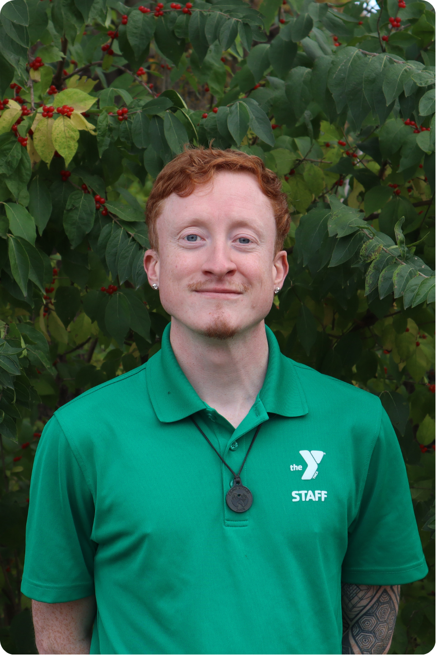 Fynn stands smiling in front of some greenery wearing a green polo