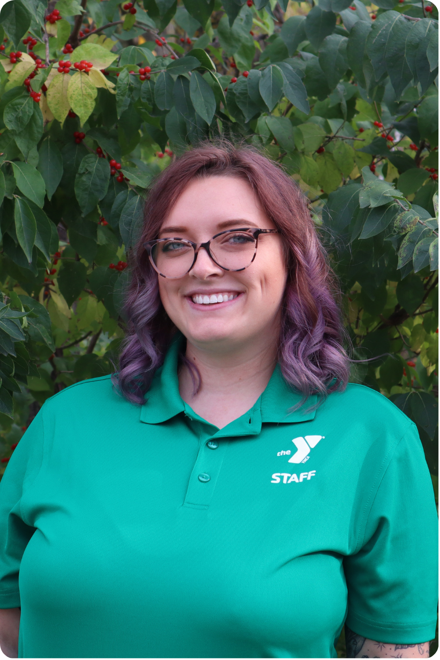 Mickie stands smiling in front of some greenery wearing a green polo