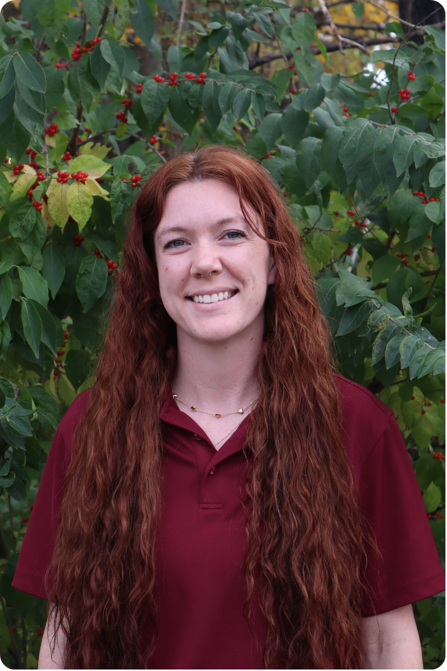 Sydney stands smiling in front of some greenery wearing a maroon polo