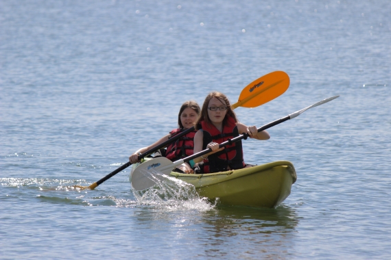 Two girls paddle a sit on top kayak on a lake.