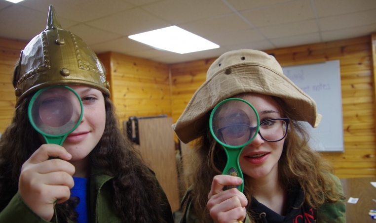 Two campers in costumes hold up magnifying glasses to their eyes.