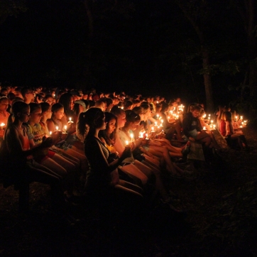 An audience sits on benches holding candles