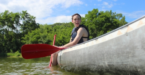 A Camper wearing a life jacket sits in a canoe preparing to practice canoe swamping 