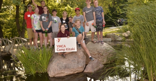 A group of kids and staff pose for a picture on rocks in the middle of a pond