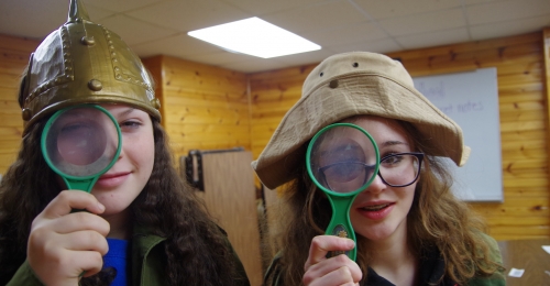 Two campers in costumes hold up magnifying glasses to their eyes.