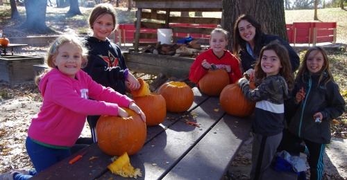 5 campers and a staff member begin to carve pumpkins on a picnic table