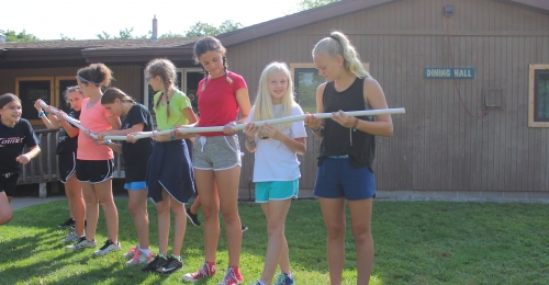 A group of campers work together to role a marble from one place to another each holding a section of tube in a long line