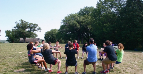 A group of teenagers all hang onto the same rope in a circle and lean back using each other for balance