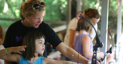 A staff member teaches a camper to shoot archery