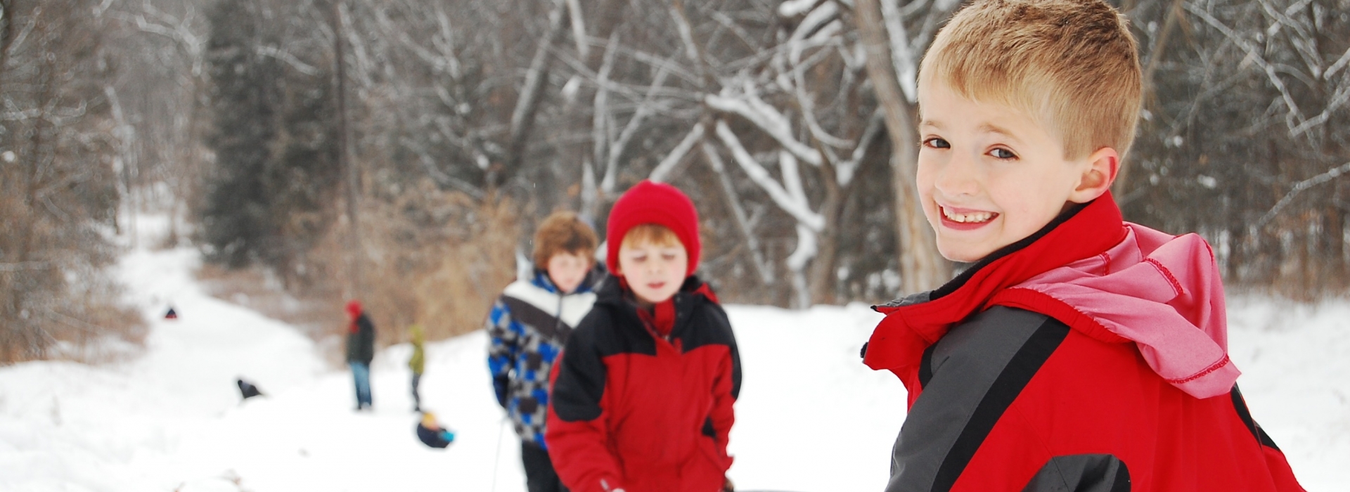 A young boy smiles over his shoulder at the top of a sled hill