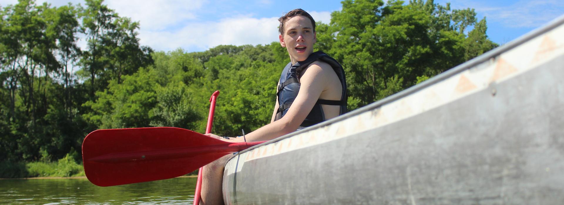 A Camper wearing a life jacket sits in a canoe preparing to practice canoe swamping 