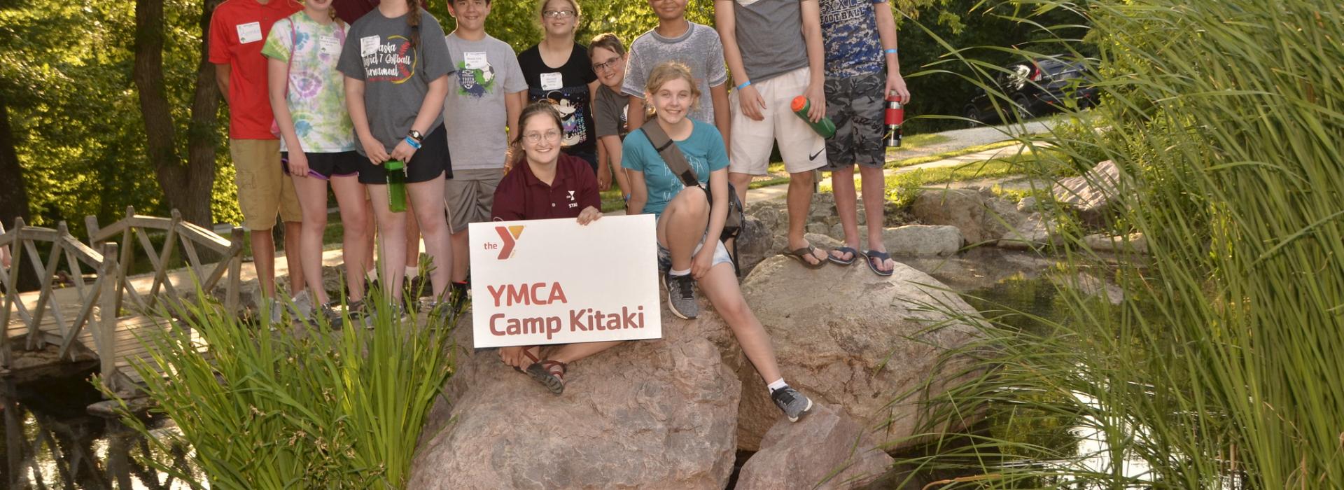 A group of kids and staff pose for a picture on rocks in the middle of a pond