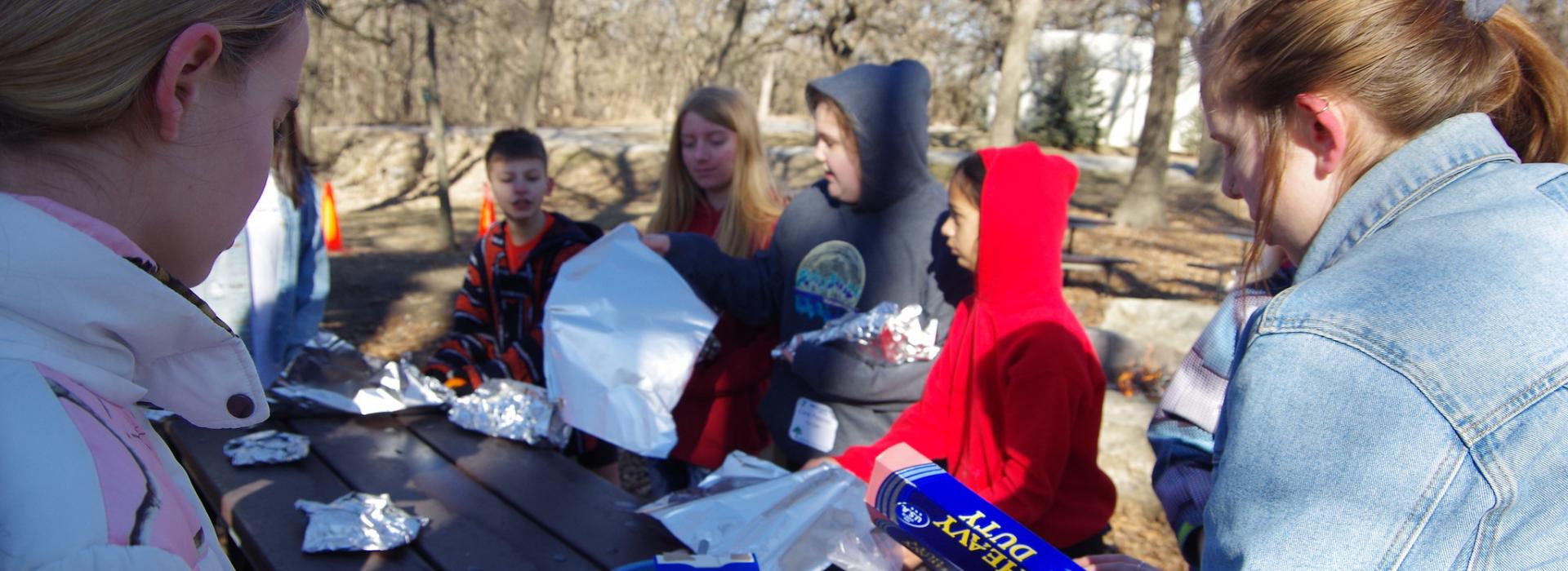 Campers prepare food around a picnic table for outdoor cooking