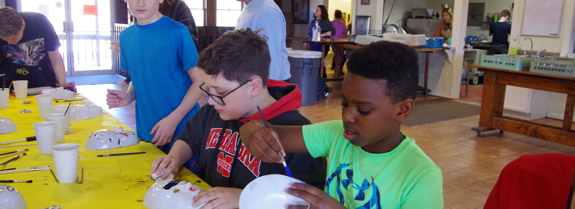 Kids sit at a table and paint masks
