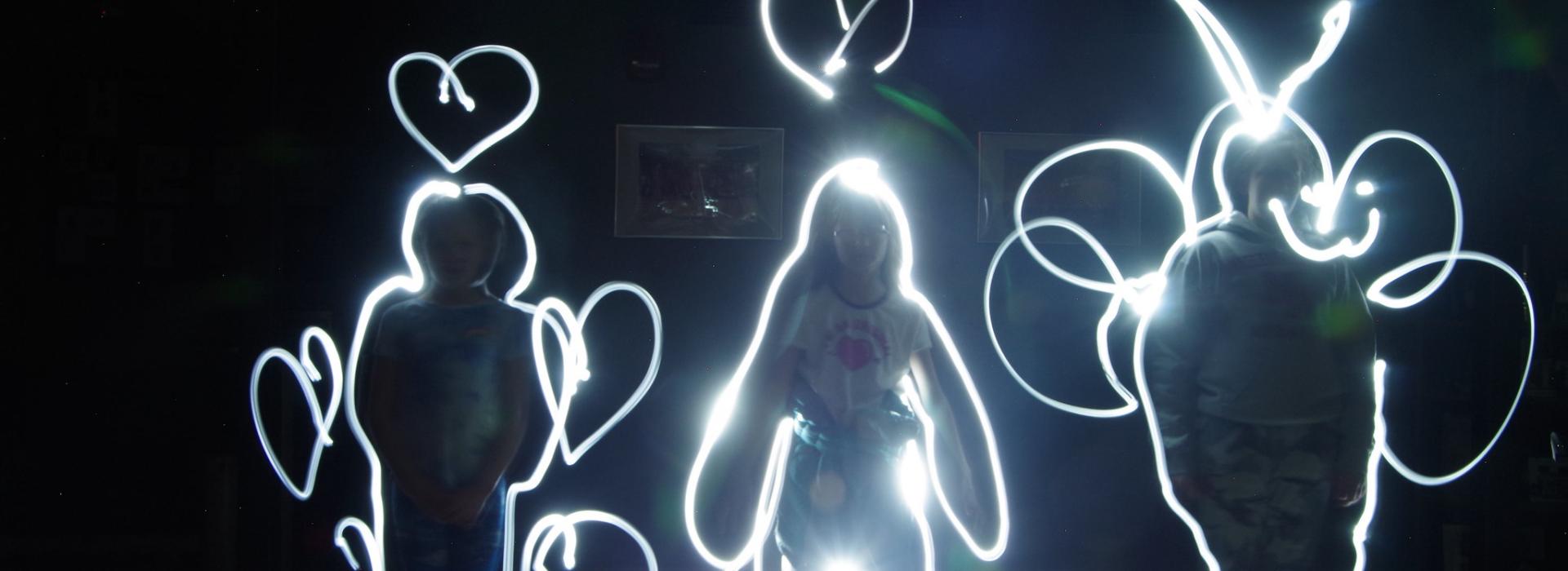 Three campers stand facing the camera and flashlights are used to trace their outlines in glowing light