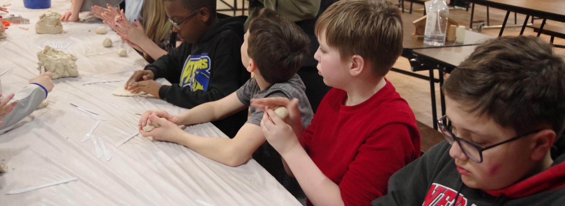 Kids sit at a table and work with clay