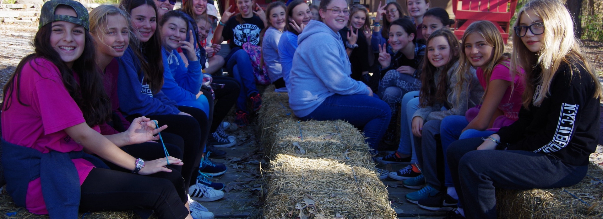 A group of campers smile at the camera while sitting on hay bales on a hay rack ride.