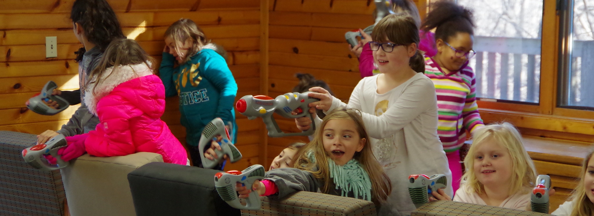 Campers smile as they use a line of chairs for defense and play laser tag