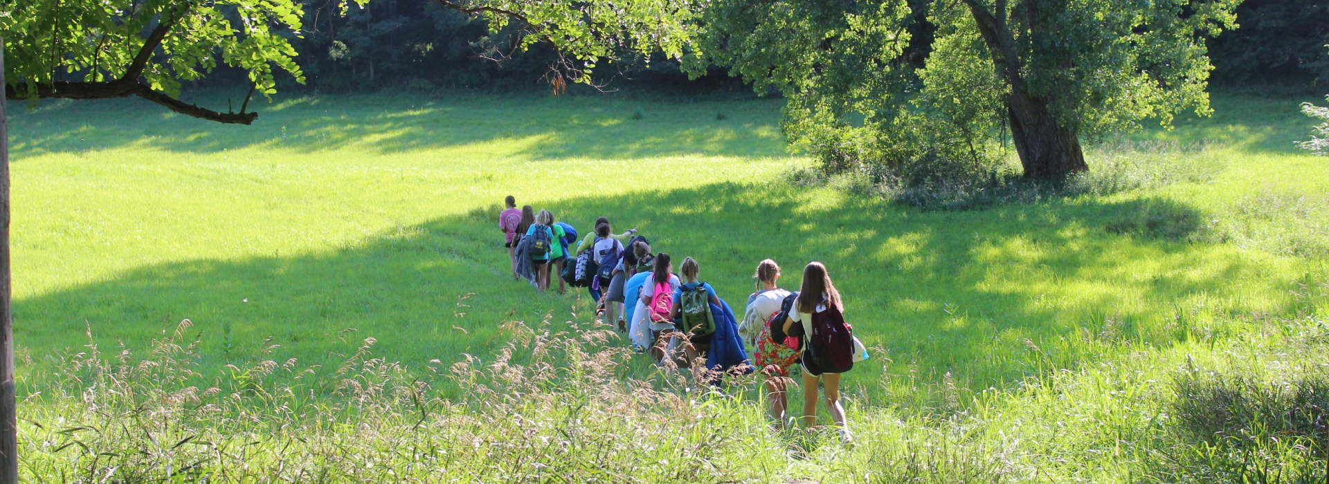 Trailblazers Campers walk in a line through a green field on their way to a campout location