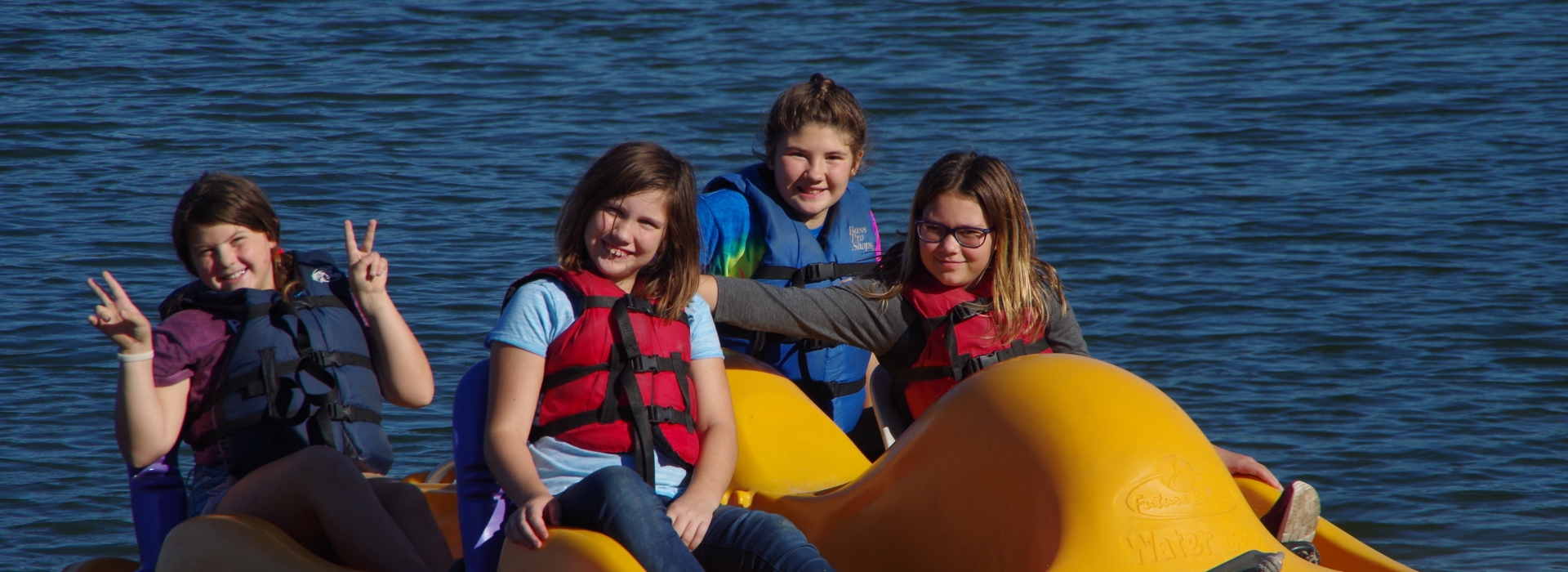 4 campers smile as they use a paddle boat on the lake