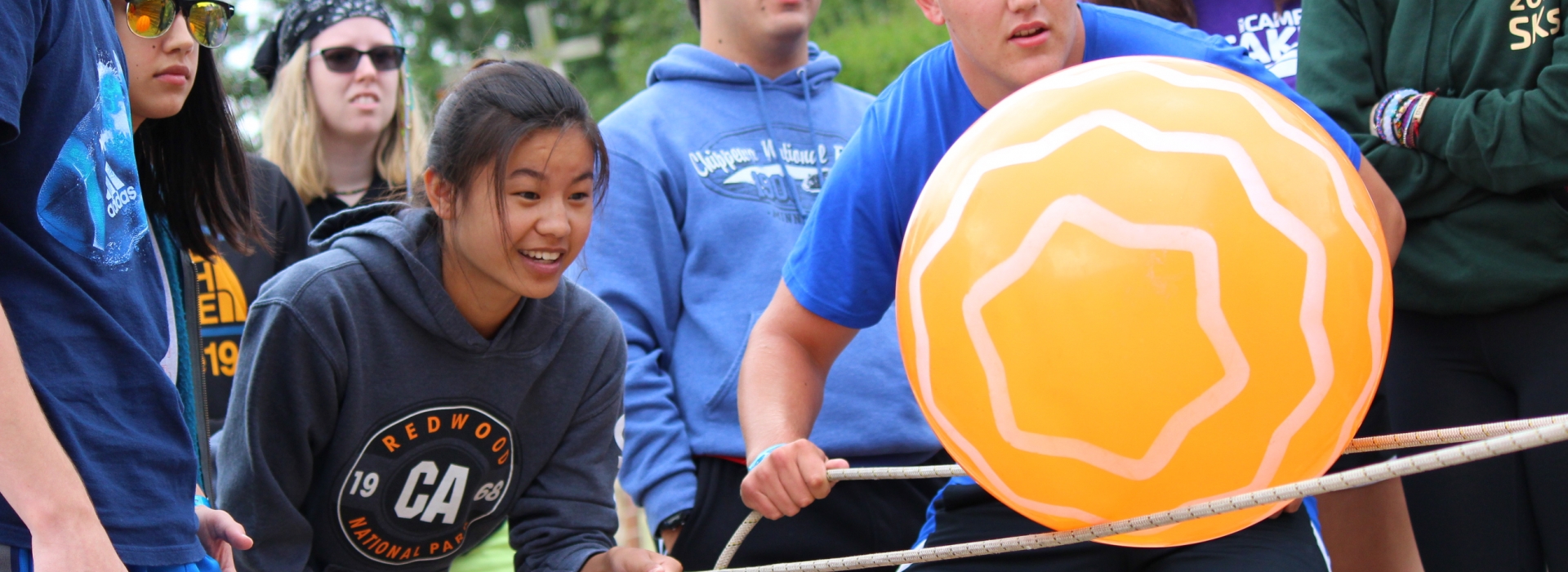 Campers concentrate on supporting a large playground ball on ropes as they complete a teambuilding challenge