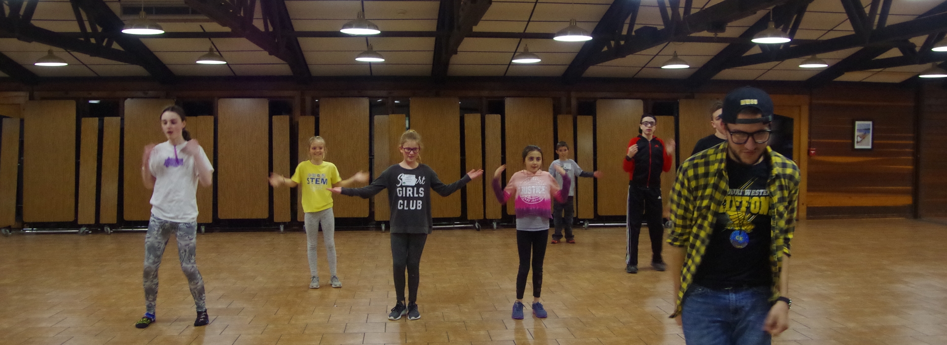 A staff stands in the foreground and teaches campers a dance routine
