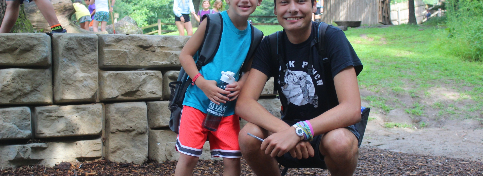 A counselor kneels by one of his campers in our natural play area