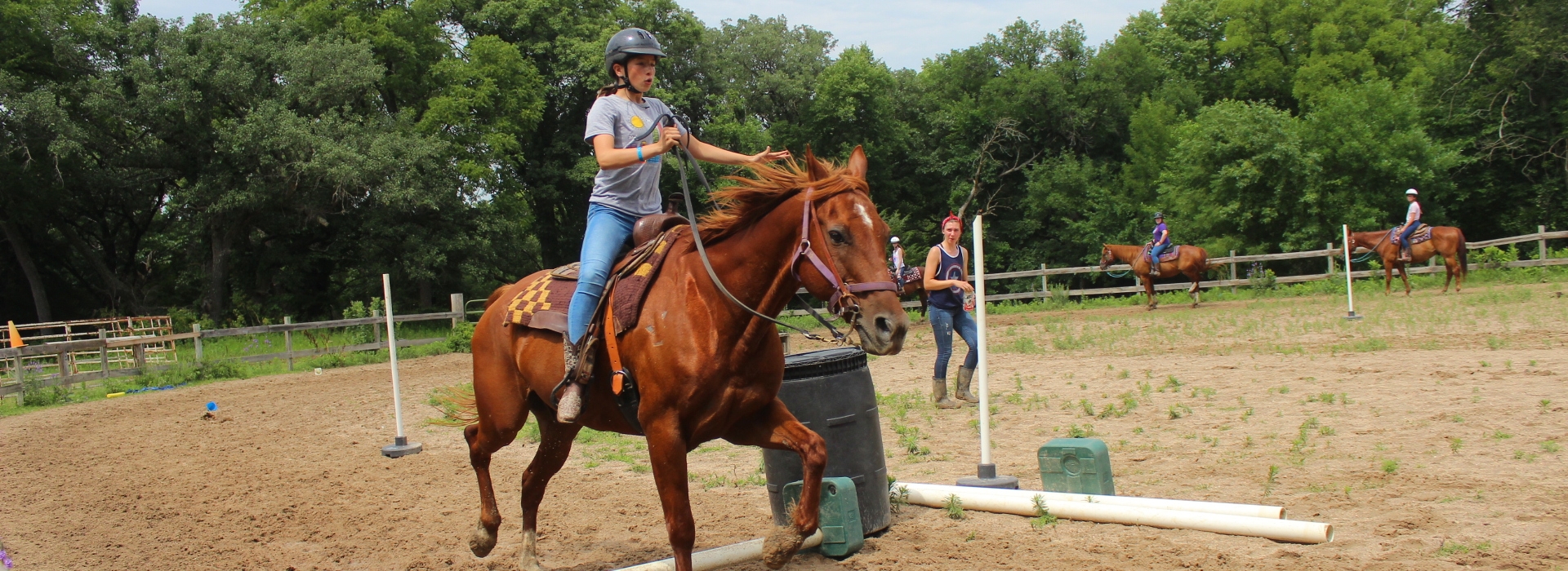 A camper guides their horse over a small jump in our arena