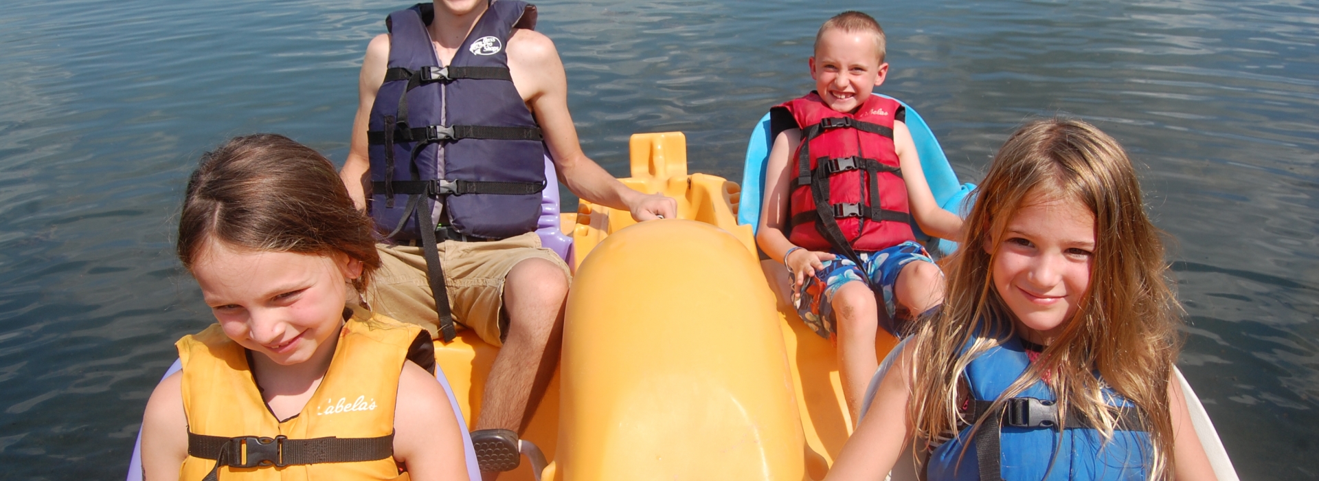 Three campers and a teen volunteer paddle on the lake in a paddle boat