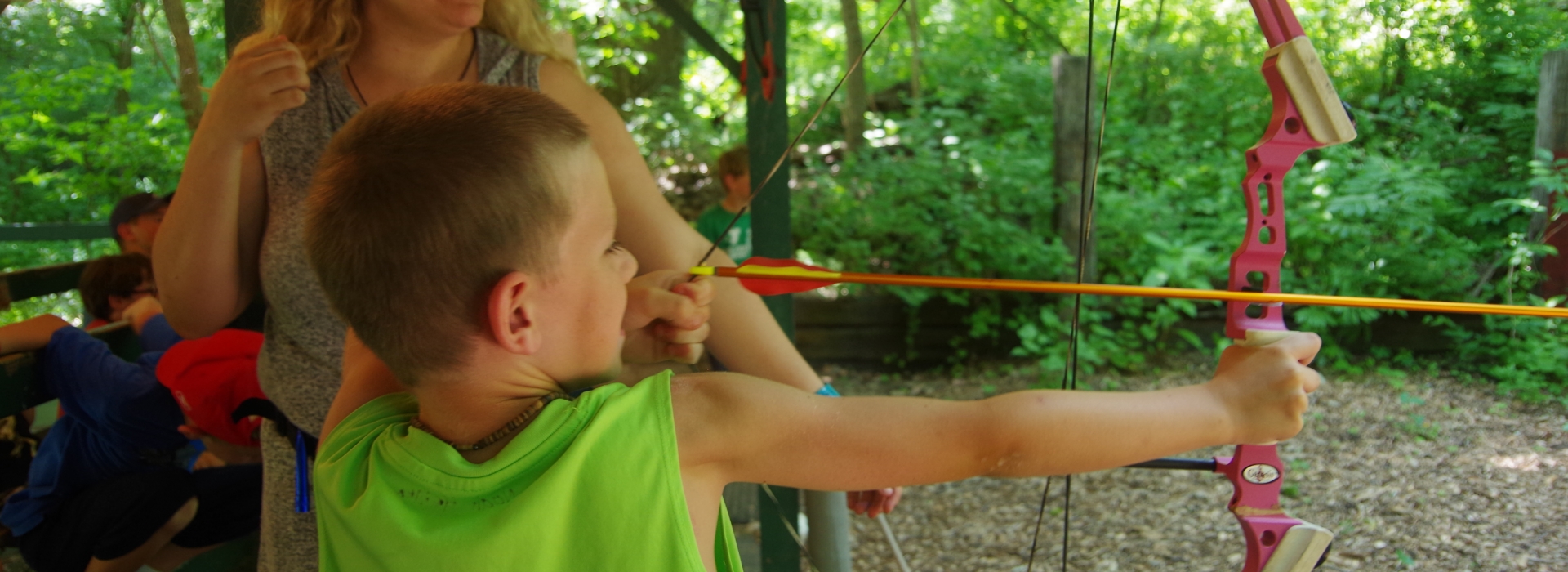 A kid smiles as he draws back an arrow
