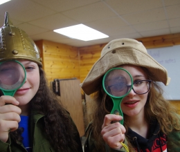 Two campers in costumes hold up magnifying glasses to their eyes.