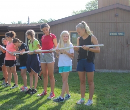 A group of campers work together to role a marble from one place to another each holding a section of tube in a long line