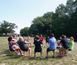 A group of teenagers all hang onto the same rope in a circle and lean back using each other for balance