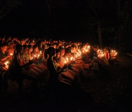 An audience sits on benches holding candles