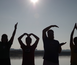 Four people make the letters YMCA with their arms as silhouettes in front of the camp lake