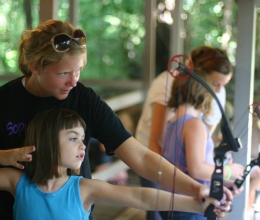 A staff member teaches a camper to shoot archery